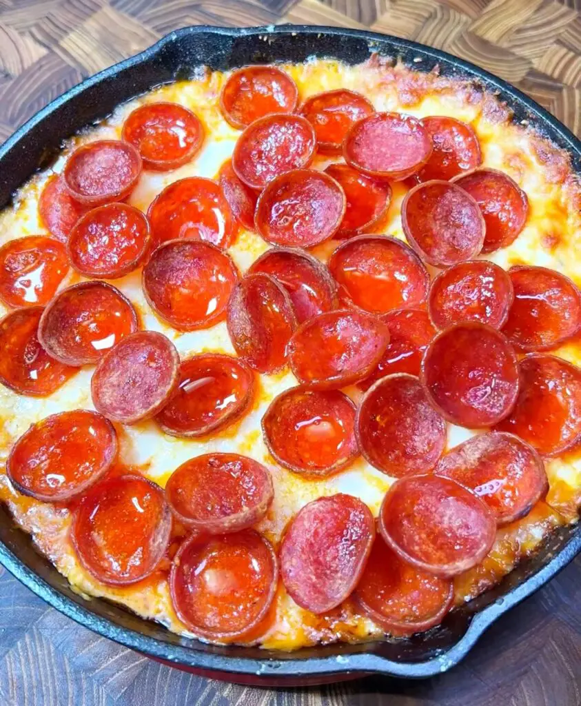 overhead view of a cast iron skillet with a pepperoni dip recipe made with cream cheese, pizza sauce, and two types of cheese.
