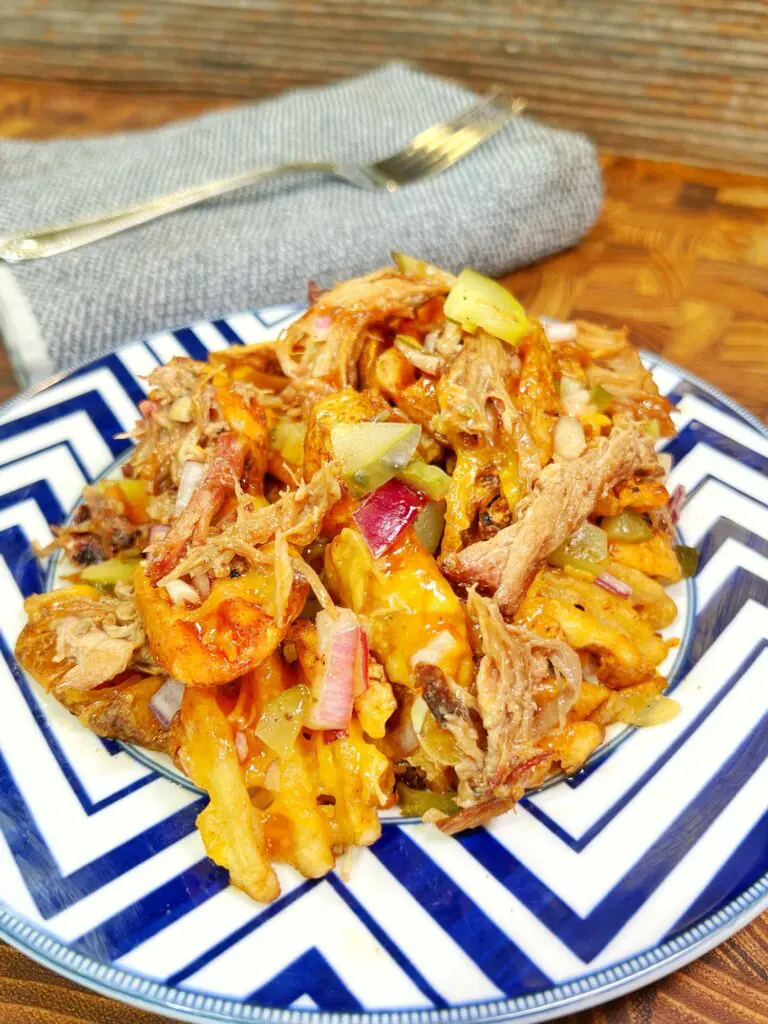 blue and white plate with loaded pulled pork fries with pickles, cheese, onion, and bbq sauce.