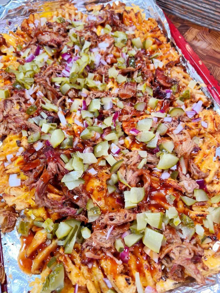 overhead view of a sheet pan with loaded fries topped with pulled pork, bbq sauce, pickles, red onion, and cheese.