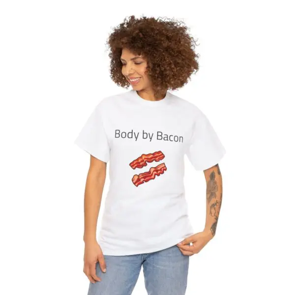 A person with curly hair is smiling and looking down while wearing a white "Body by Bacon" t-shirt, adorned with two delicious-looking strips of bacon. They are standing against a plain background.