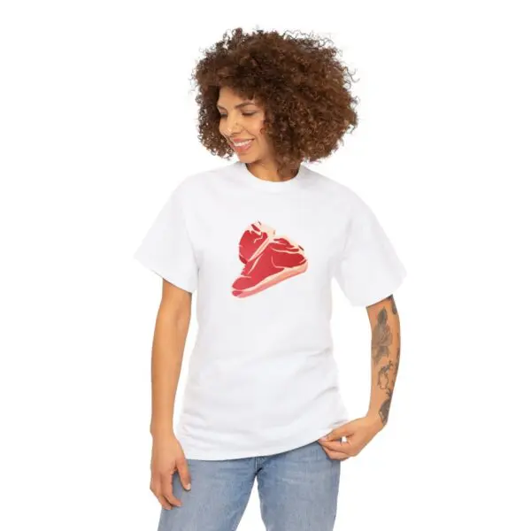 A person with curly hair smiles while wearing the Steak T-Shirt, which features a red shoe design. They have tattoos on one arm and are styled in relaxed blue jeans.