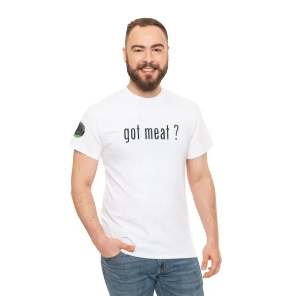 A man with a beard smiles effortlessly while wearing the "got meat ?" white T-shirt in bold black text. He pairs it with blue jeans, standing against a plain white background, capturing the perfect blend of casual and confident style.