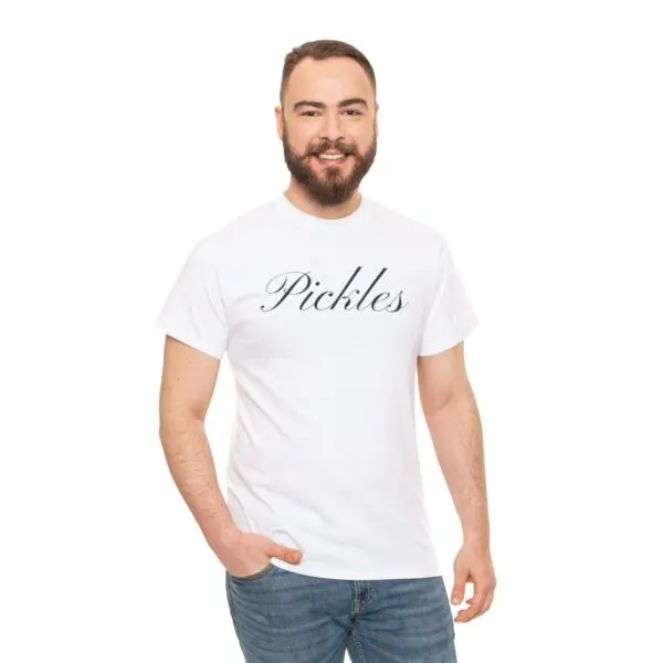 A bearded man with short hair is grinning, clad in a Pickles T-shirt featuring the word "Pickles" in script font. He embodies a feeling of delightful simplicity and stands against a plain white backdrop, casually resting one hand in his jeans pocket.