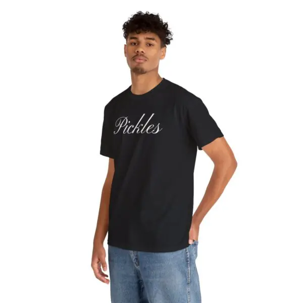 A person stands wearing the Pickles T-shirt, featuring the word "Pickles" in white script across the chest, evoking a sense of something delicious. They have short curly hair and are paired with blue jeans against a plain white background.