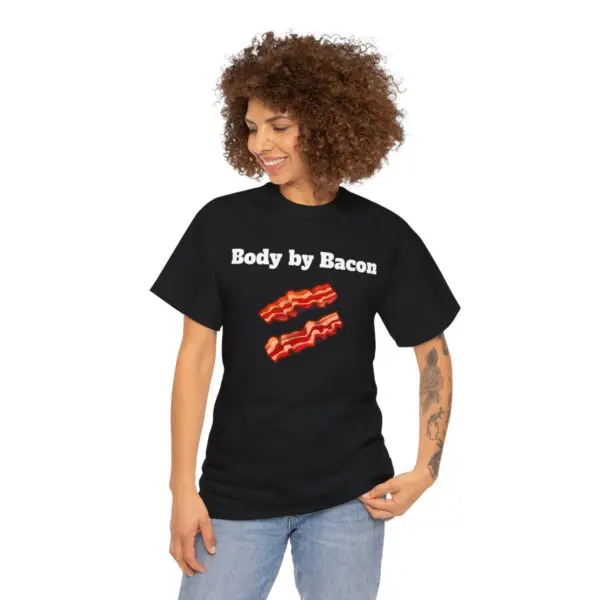 A person is smiling with one hand in their pocket while wearing a Body by Bacon black T-shirt featuring images of mouth-watering bacon strips.