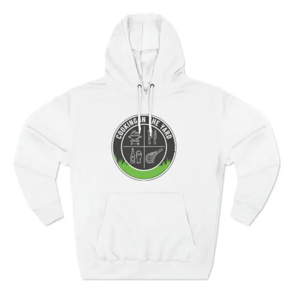 Introducing the Cooking In The Yard Hoodie: a white hoodie adorned with a circular logo on the chest. The logo highlights grilling utensils, a grill, a bottle, and a steak with green and black accents, complemented by the text COOKING IN THE YARD—ideal for fans of effortless and delicious backyard barbecues.