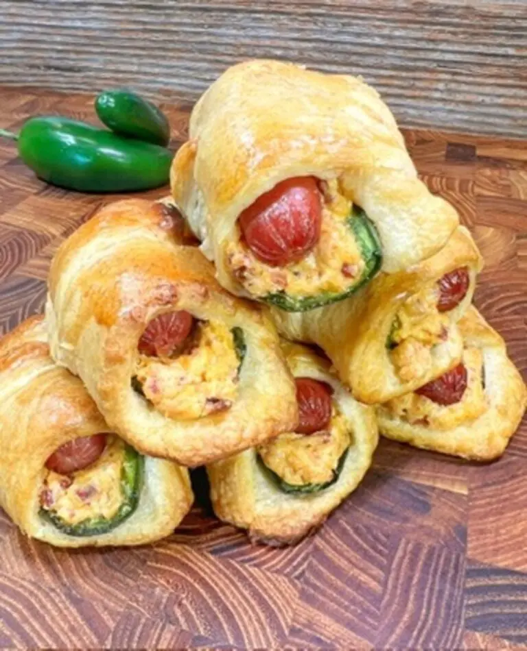 A stack of golden-brown pastries, perfectly stuffed with jalapeños, cheese, and sausages, is displayed on a wooden surface. Two whole jalapeños are in the background, making this tasty treat an easy delight for any spicy food lover.