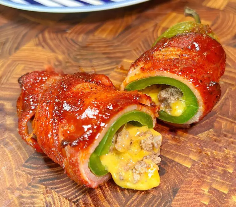 Two bacon-wrapped jalapeño poppers sit on a wooden surface, cut open to reveal an easy, savory filling of melted cheese and ground meat inside the green peppers. The bacon appears perfectly crispy and glazed.