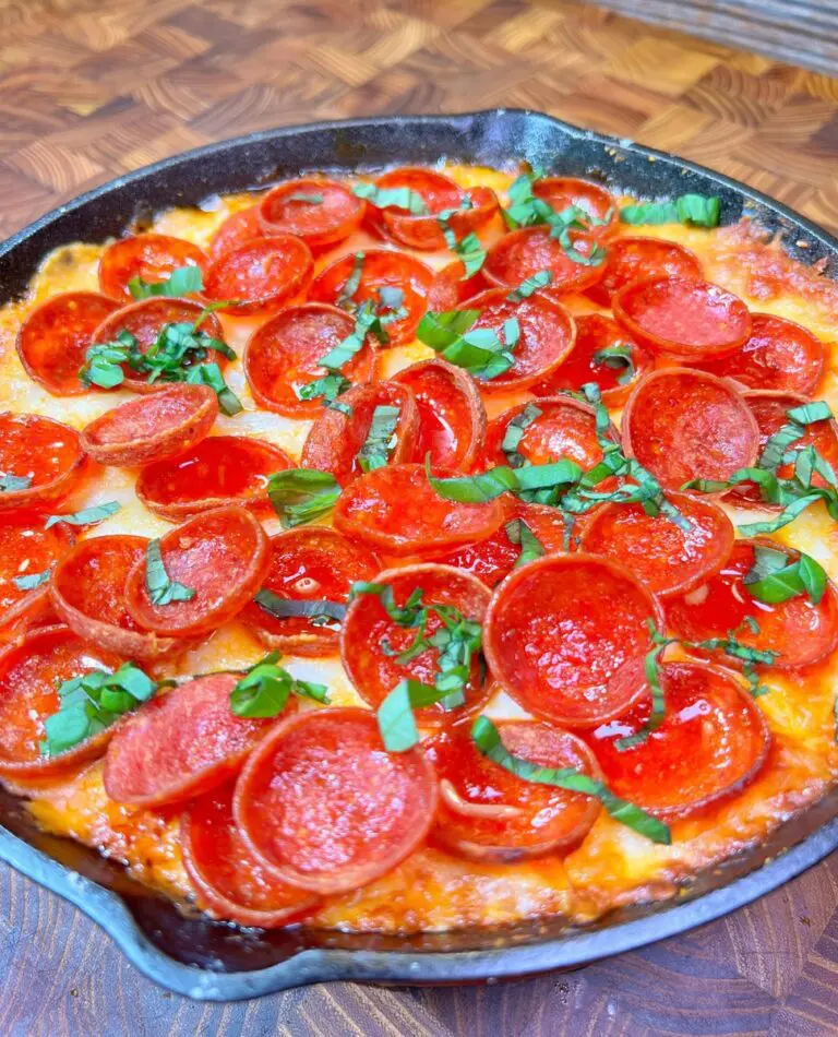 A skillet brimming with a freshly baked pizza, topped with zesty pepperoni slices and sprinkled with fresh basil leaves, sits invitingly on a wooden table. The golden-brown crust and gooey melted cheese make it perfect for an indulgent dip combo.