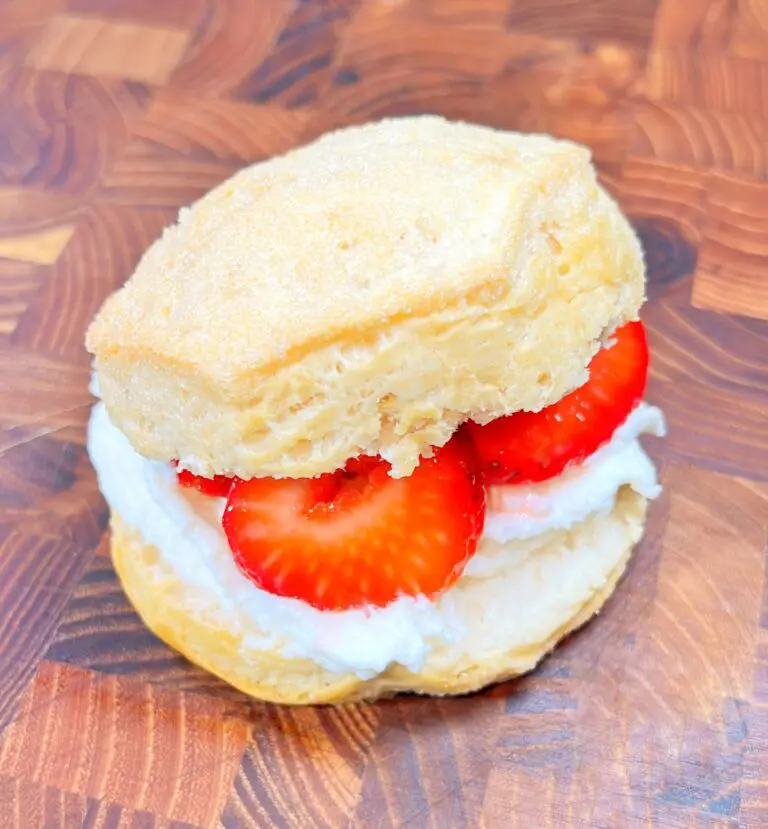 A biscuit split open with whipped cream and fresh strawberry slices inside, creating a delicious treat placed on a wooden surface.