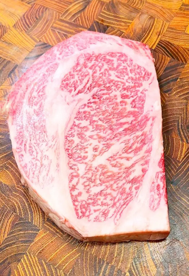 A marbled piece of Wagyu beef on a textured wooden cutting board, displaying intricate patterns of fat interspersed within the meat.