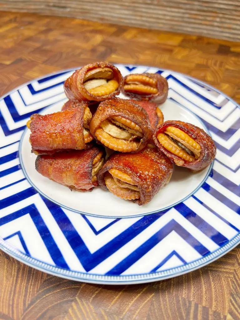 A plate of pecan-stuffed dates wrapped in crispy bacon, served on a blue and white zigzag-patterned dish. The wooden background adds warmth to the presentation.