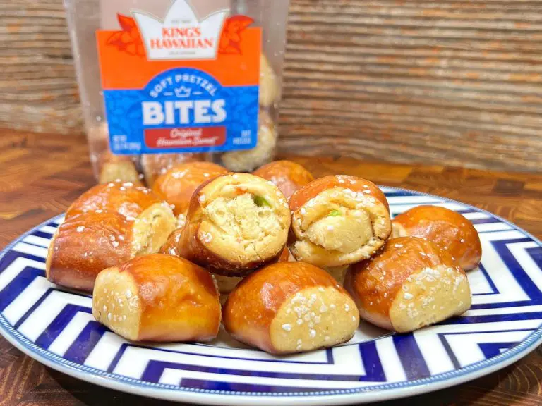 A plate of Kings Hawaiian soft pretzel bites is arranged on a geometric-patterned blue and white plate. The golden brown pretzel bites are sprinkled with salt, and an open package is visible in the background on a wooden surface.