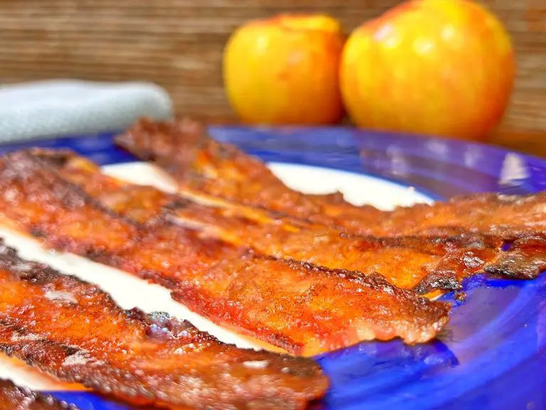 Crispy bacon strips on a blue plate with two apples in the background.