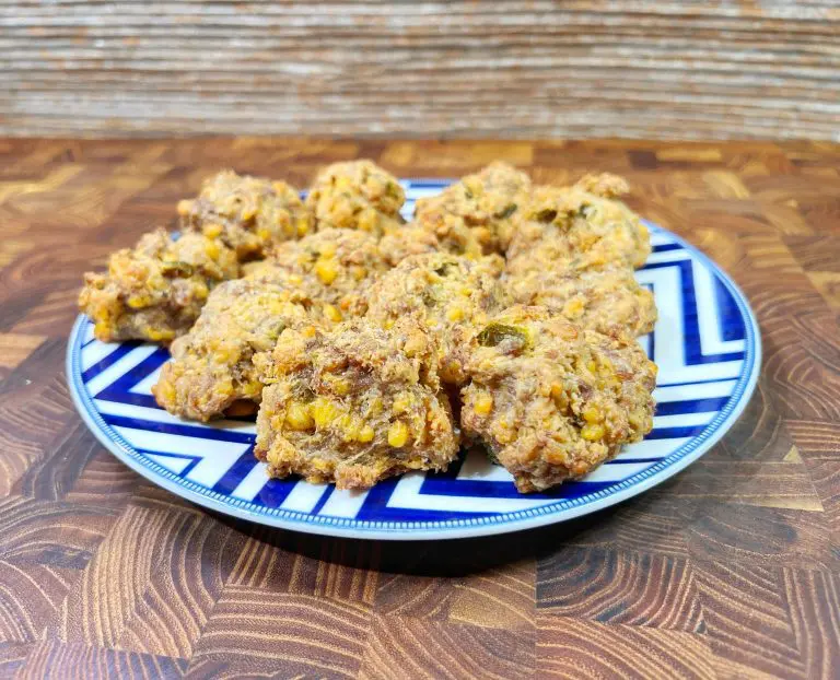 A plate of homemade cookies with visible corn kernels and nuts, placed on a blue and white patterned plate. The background features a textured wooden surface.