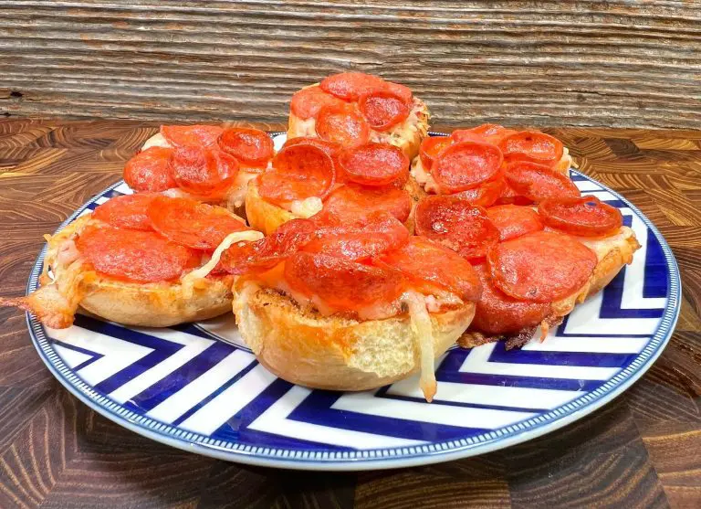 A plate of mini pepperoni pizzas on a blue and white patterned dish. Each pizza is topped with melted cheese and pepperoni slices, set against a wooden background. homemade pizza recipe