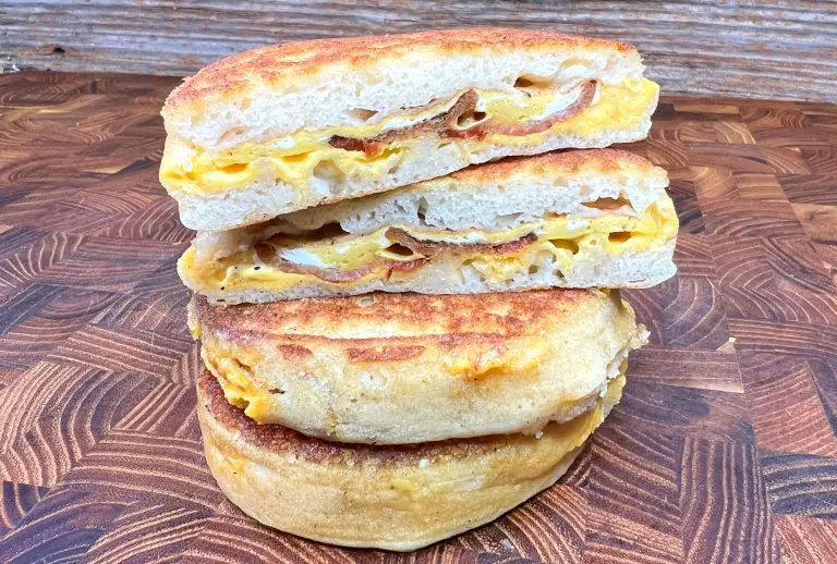 A stack of two tasty paninis filled with melted cheese and thin slices of bacon, cut in half and perfectly placed on top of each other. The paninis have a crispy, golden-brown crust and are set against a wooden background.