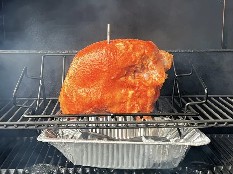 A smoked turkey breast sizzles on the grill, perched elegantly on a rack above a foil tray. A temperature probe ensures perfect doneness, while fragrant smoke swirls around the succulent meat, enhancing its rich flavor.