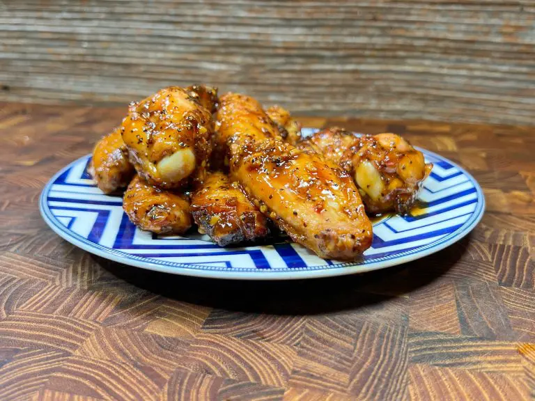 A plate of glazed chicken wings with herbs is set on a wooden surface. The plate has a blue and white geometric pattern.