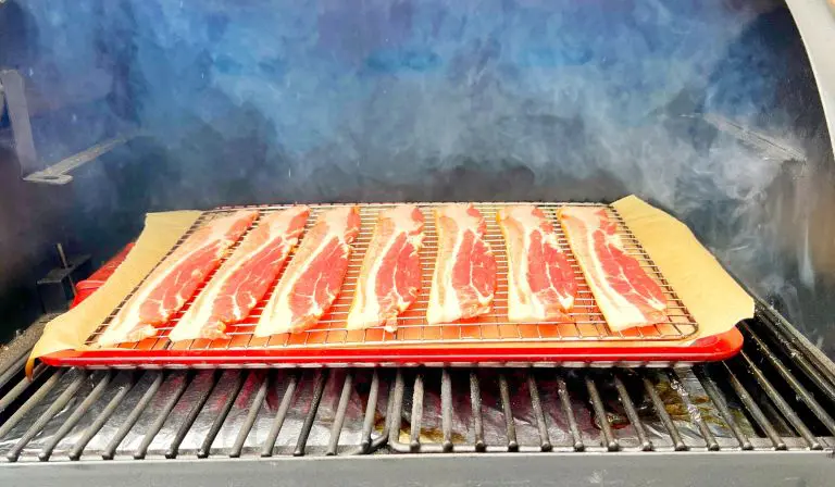 Slices of bacon are placed on a rack inside a smoker, with visible smoke swirling around.