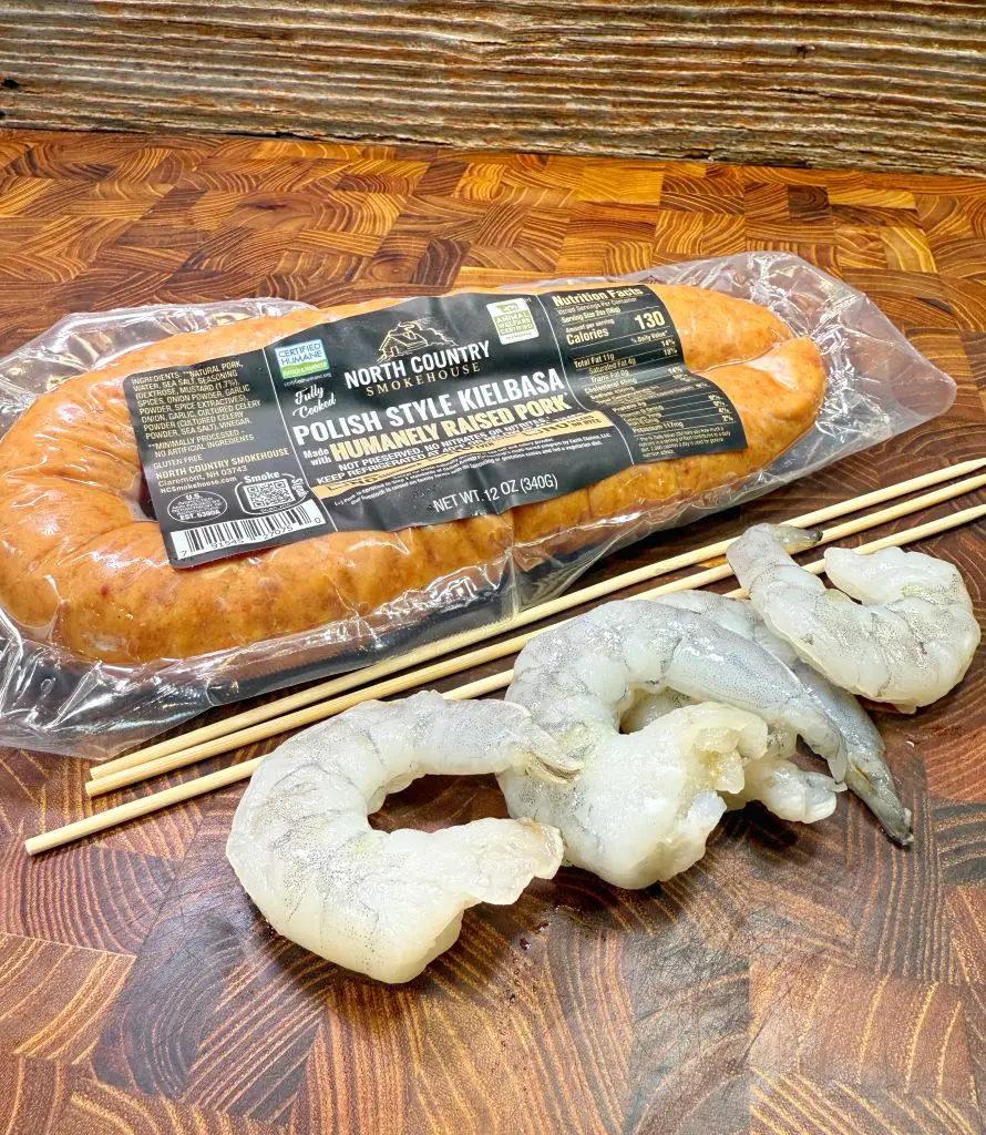Package of Polish style kielbasa on a wooden surface, alongside raw shrimp and wooden skewers.