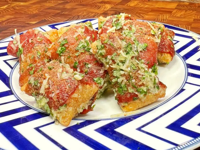 Five pieces of crispy tomato-topped pizza rolls garnished with fresh herbs and grated cheese, served on a blue and white patterned plate on a wooden table.