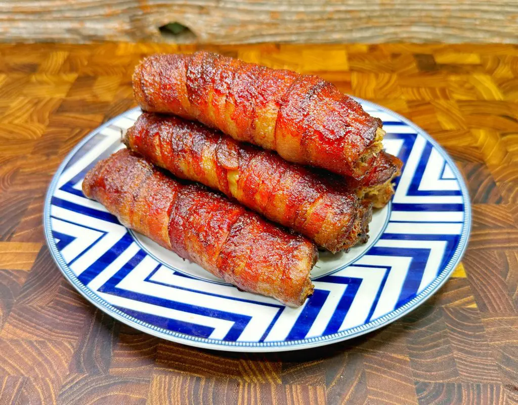 a plate with a stack of bacon wrapped texas twinkies with manicotti pasta shells, cream cheese, brisket, cheese, and jalapenos.