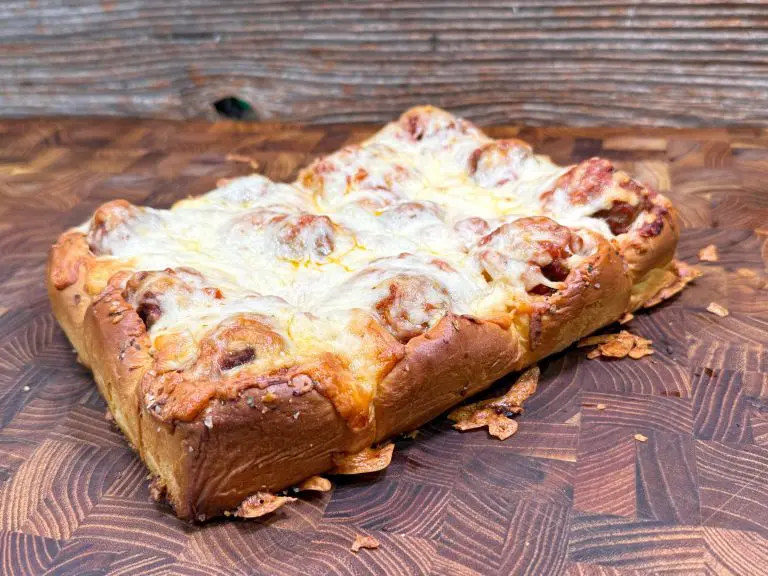 A baked square of cheesy bread with browned cheese on top, placed on a wooden textured surface.