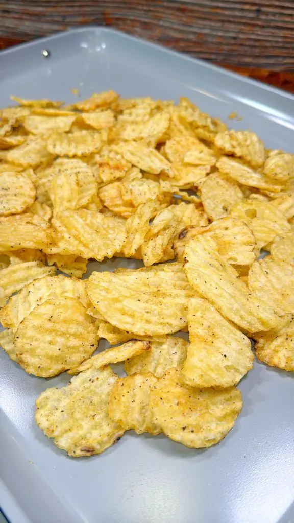 Ruffled potato chips seasoned with black pepper are scattered across a gray surface.