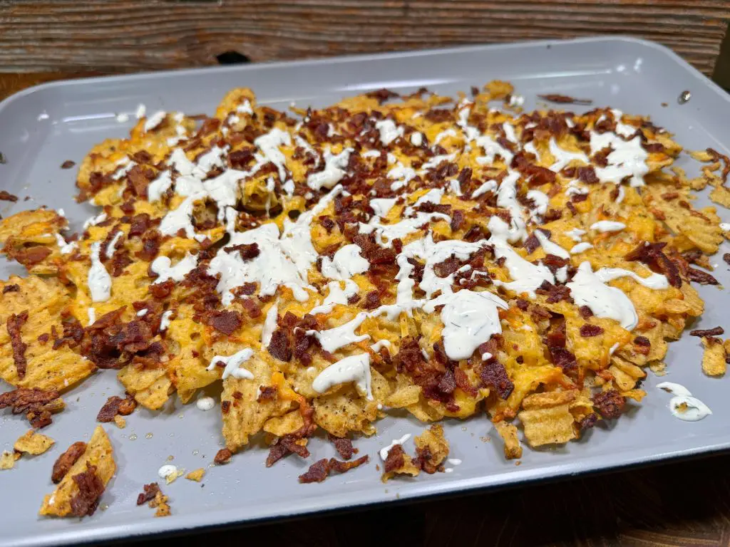 A tray of nachos topped with melted cheese, crumbled bacon, and drizzled with a white sauce, likely sour cream or ranch dressing. The tray sits on a wooden surface.