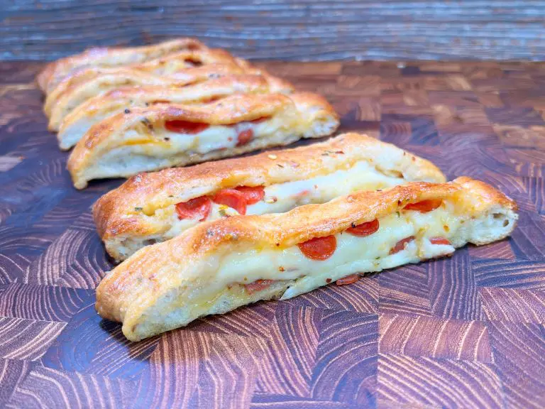 Sliced, baked bread loaves filled with melted cheese and small pepperoni pieces displayed on a wooden surface. The bread has a golden-brown crust with a crispy texture.