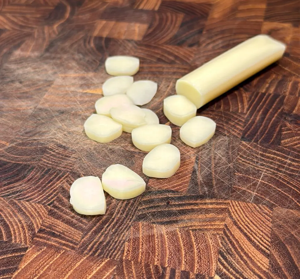 Sliced pieces of garlic stem scattered on a wooden cutting board with a geometric pattern.