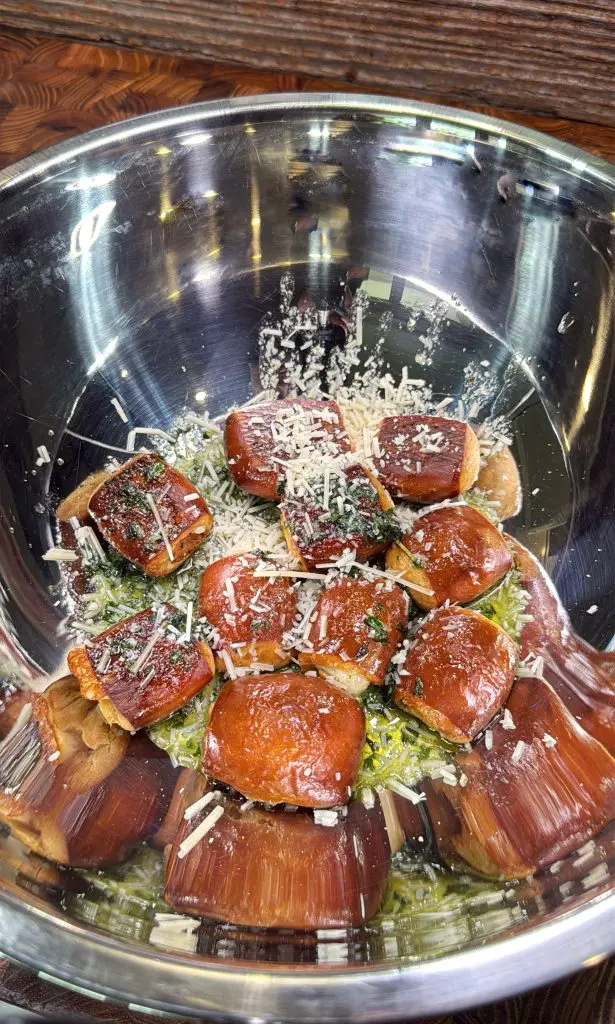 A metal bowl filled with a salad topped with several glazed, breaded bites, garnished with grated cheese and herbs. The bowl sits on a wooden surface.