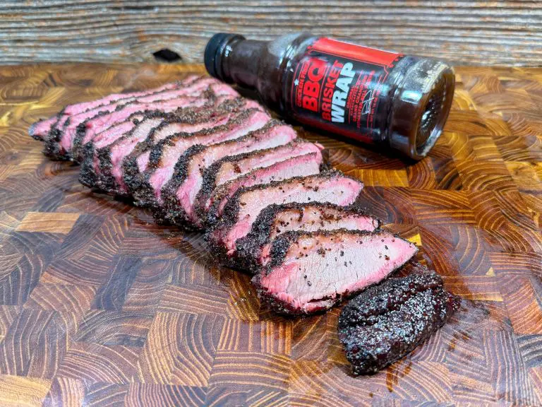 Sliced, juicy smoked meat with a peppery crust is arranged on a wooden cutting board. A bottle labeled “BBQ Wrap” lies in the background, partially on its side.
