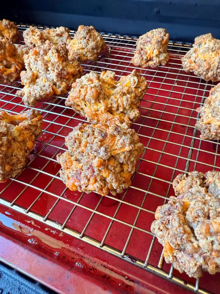 Roughly shaped, golden-brown biscuits with visible cheese and on the garlic cheeseburger bites cooling on a wire rack over a red tray.