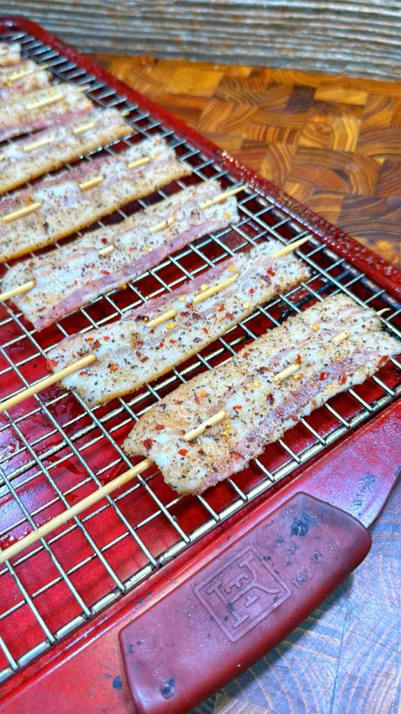 Several skewers of seasoned fish fillets are arranged on a wire rack over a red baking sheet, ready for grilling or roasting. The fish is sprinkled with red chili flakes and spices.
