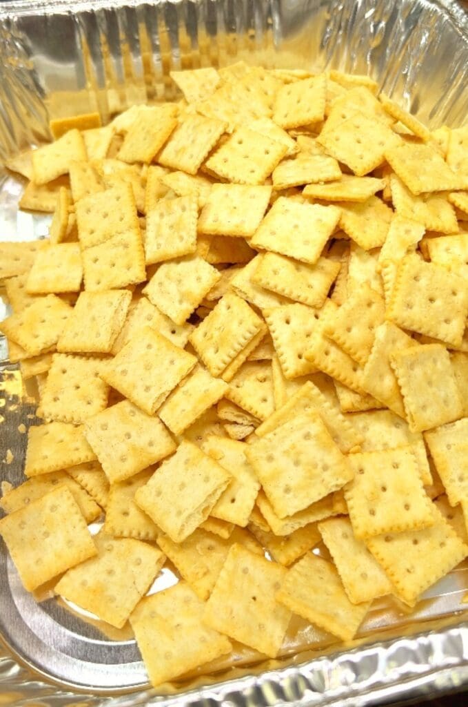 A close-up of a tray filled with Saltine crackers for making dill pickle saltines on a metallic and rectangular.