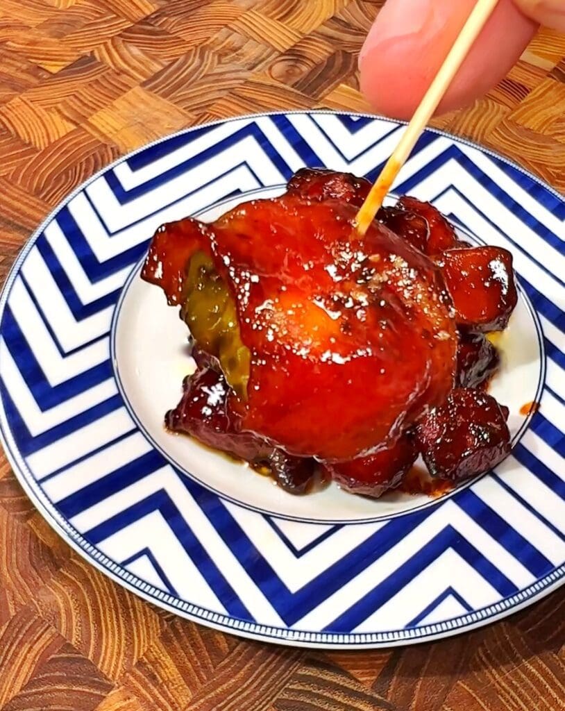 a small plate with a bacon wrapped pickle bites coated in a sweet glaze and held by a toothpick.