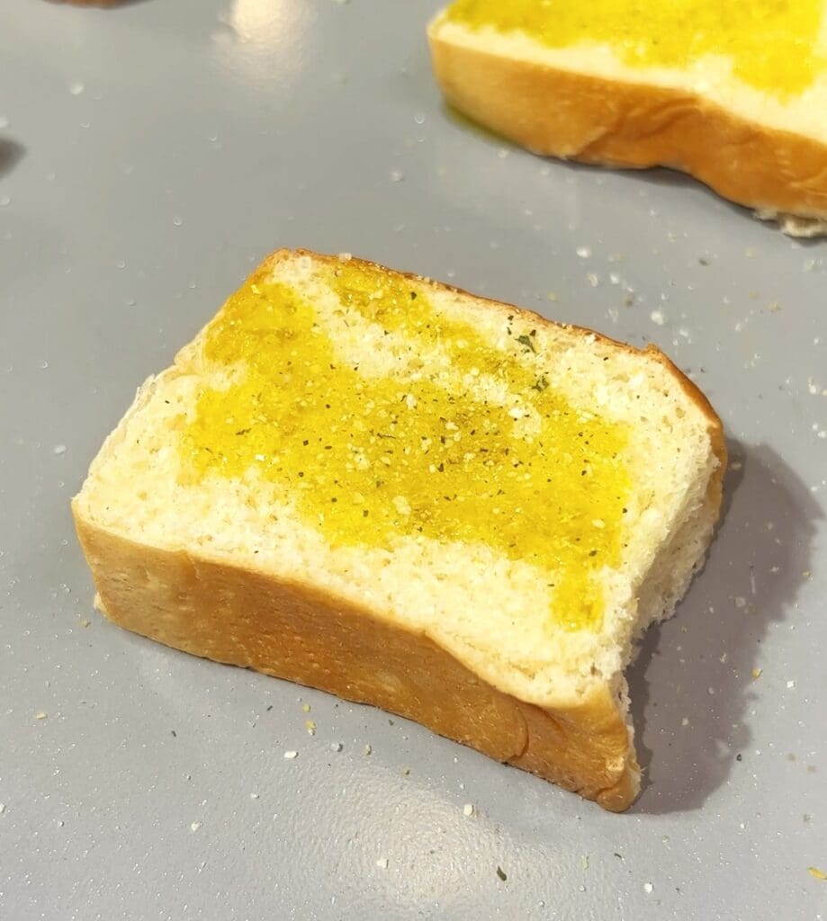 A slice of bread covered with melted butter and sprinkled with black pepper sits on a gray surface. Another slice is partially visible in the background.