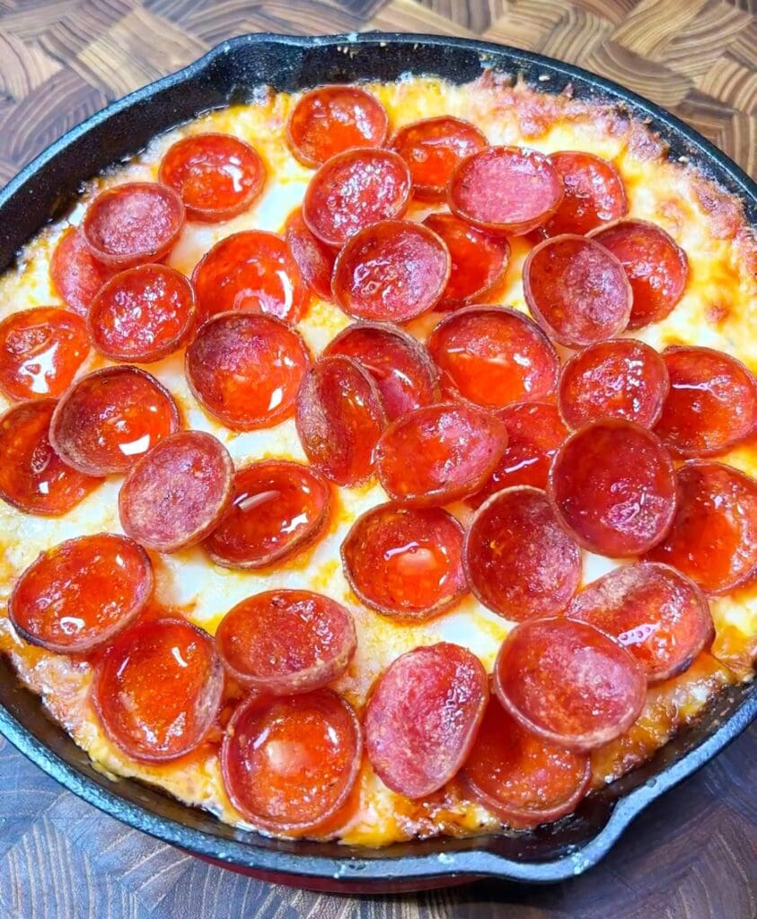 overhead view of a cast iron skillet with a pepperoni dip recipe made with cream cheese, pizza sauce, and two types of cheese.