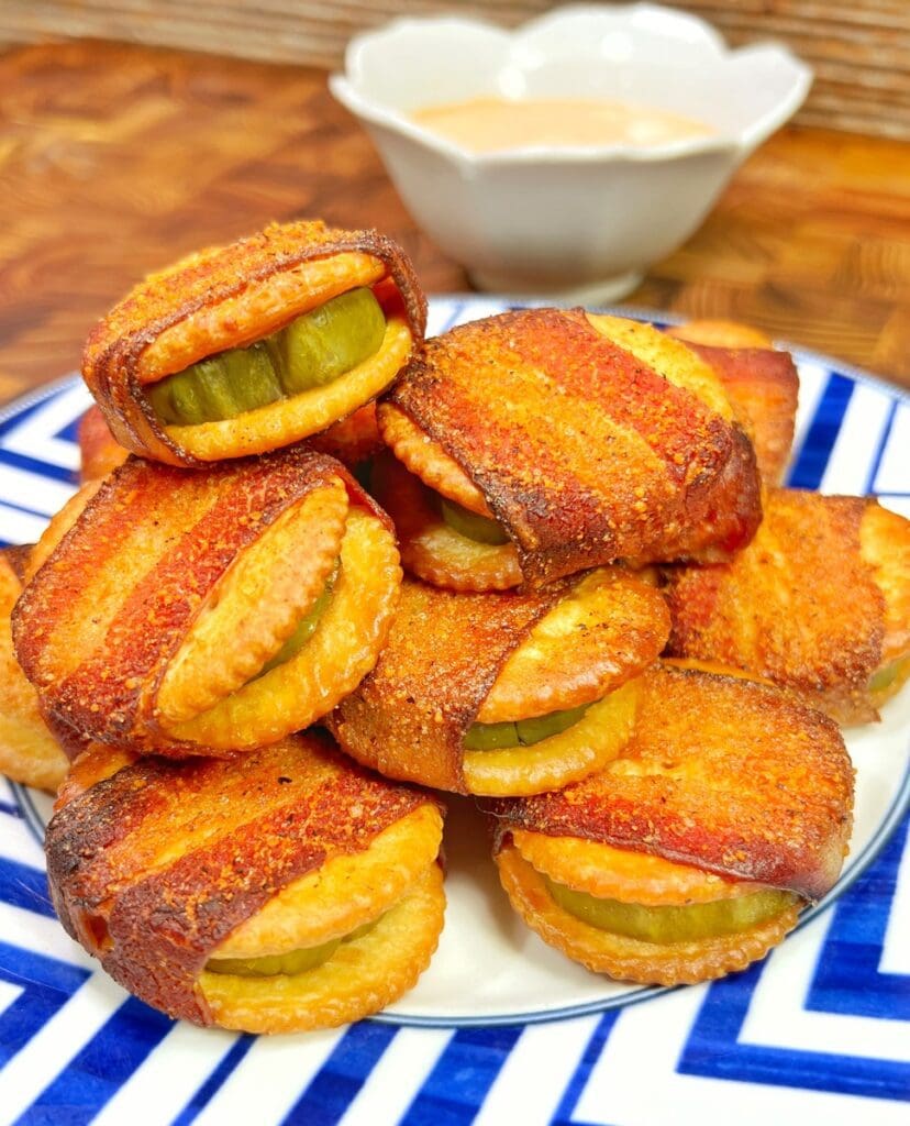 blue and white plate with smoked ritz crackers wrapped in bacon with pickle bites next to a bowl of dip.