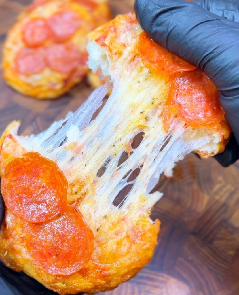 Close-up of a gloved hand stretching a cheesy, cheesy stuffed biscuit with pepperoni.