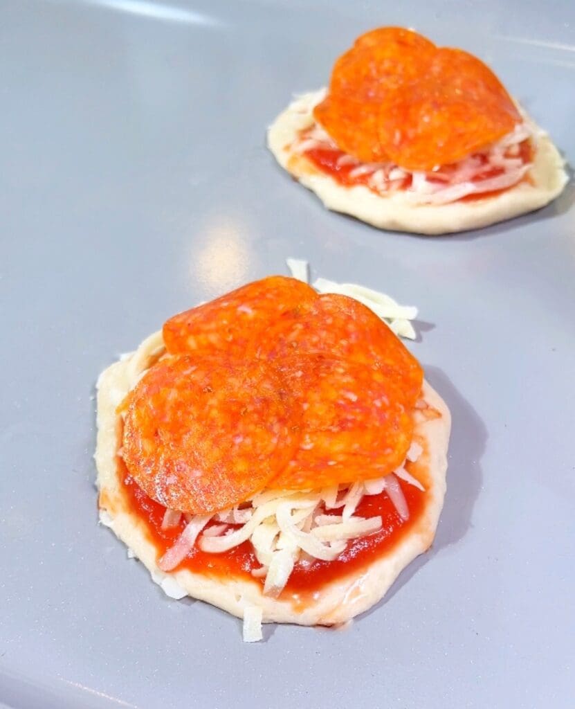 Two uncooked mini stuffed biscuits filled with mozzarella, pepperonis, and pizza sauce.