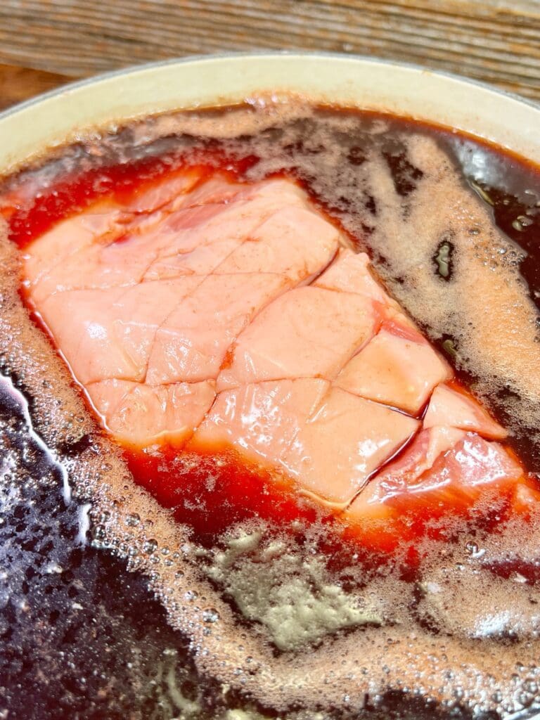 Close-up of a piece of raw pork butt marinating in cherry dr. pepper before smoking and turning into pulled pork.