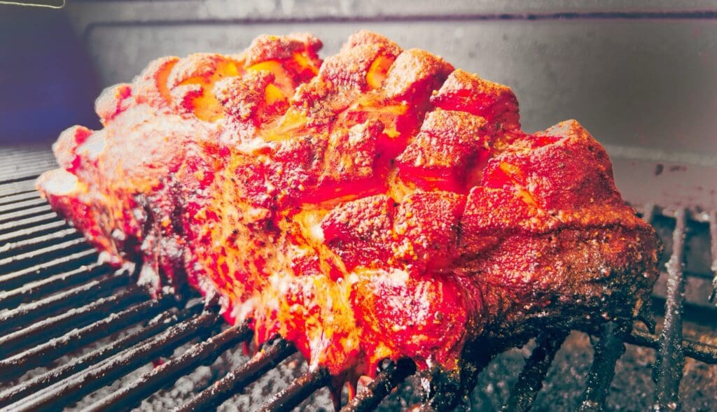 close up view of dr. pepper infused pork on a smoker to make pulled pork for loaded fries and more.