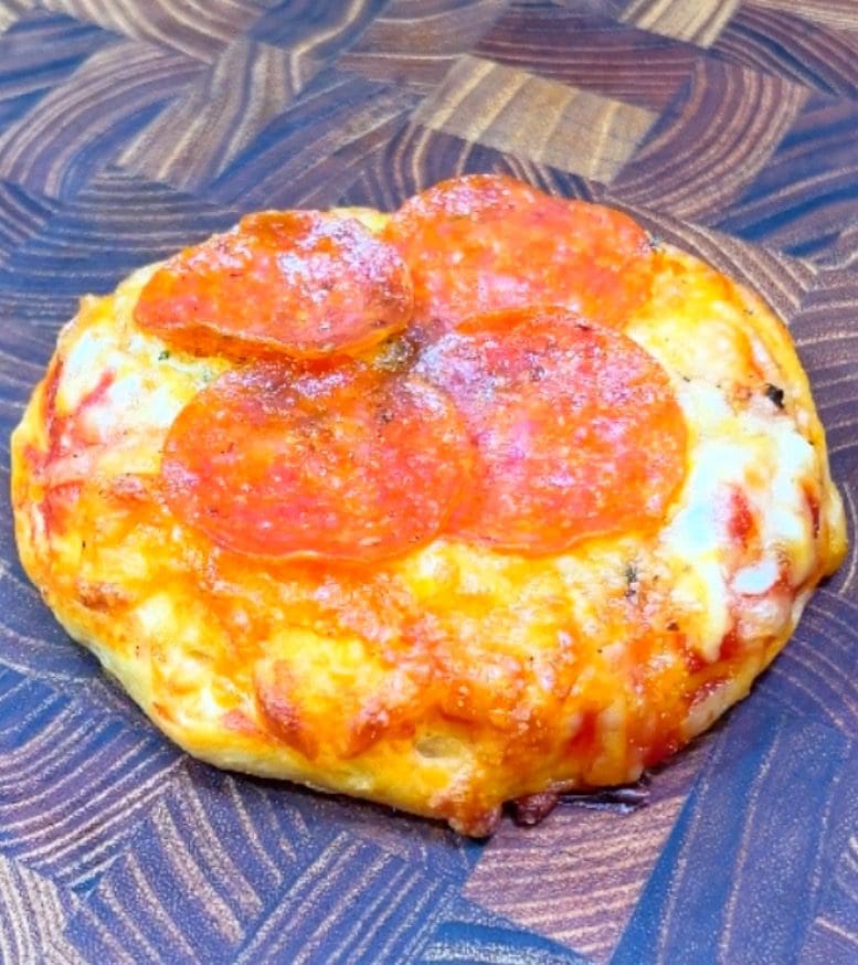 A delicious small pepperoni pizza with melted cheese and three slices of pepperoni sits perfectly on a dark wooden surface.
