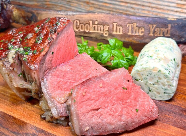 sliced beef tomahawk steak next to whiskey infused compound butter with garlic and shallots.