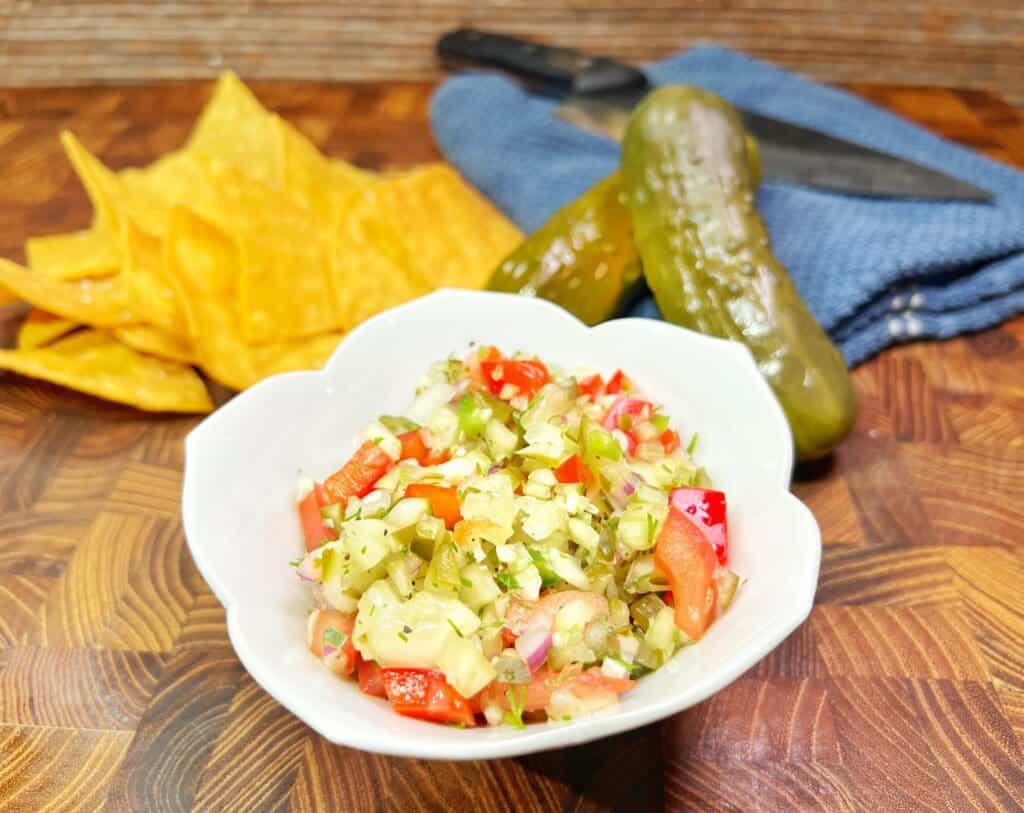 white serving dish with homemade pickle salsa or pickle de gallo by tortilla chips and pickles.