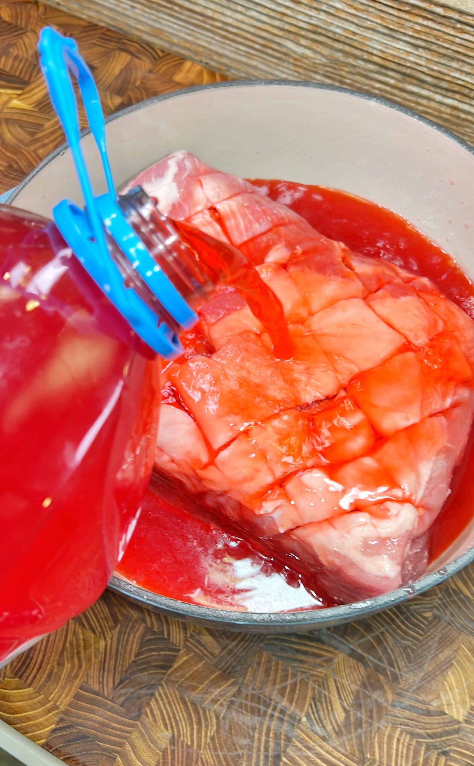 A large piece of raw pork butt is scored and being marinated to make Hawaiian Punch pulled pork.