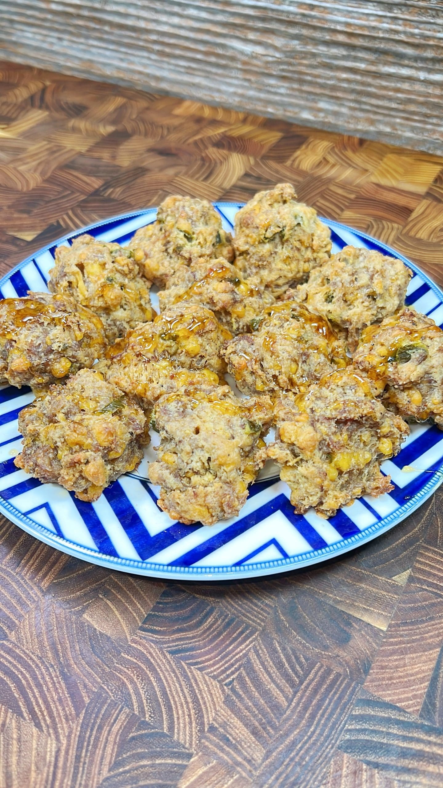 A blue and white patterned plate filled with a dozen baked savory sausage balls, placed on a wooden surface. The sausage balls are golden brown with visible herbs and crispy bits.